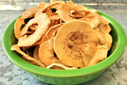 A green bowl filled with dried honeycrisp apple chips on a kitchen countertop.